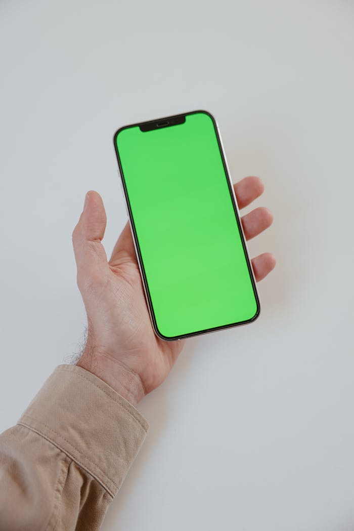 creative-02 Close-up of a hand holding a smartphone with a green screen, ideal for mockup and design presentations.